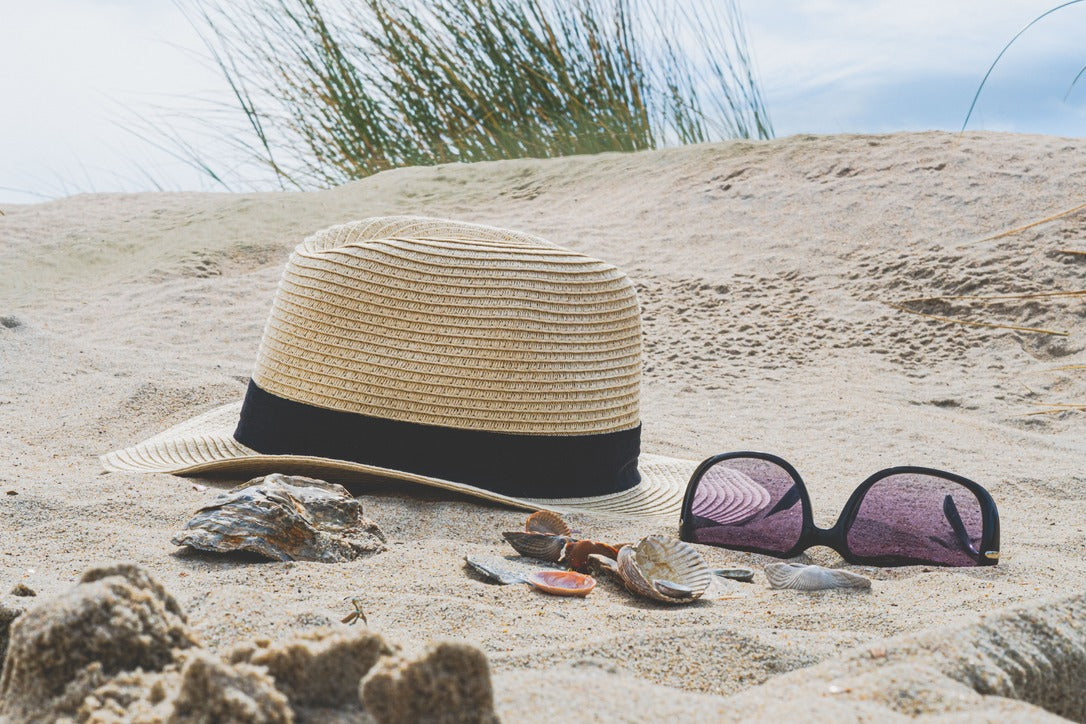 A Fedora, Sunglasses and seashells sitting on a beach