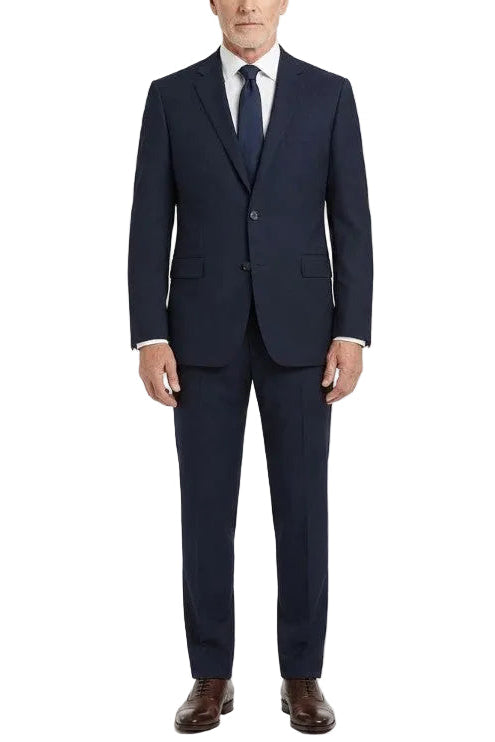 A man wearing a navy blue two-piece suit with a white dress shirt and a dark tie, standing against a plain white studio background.