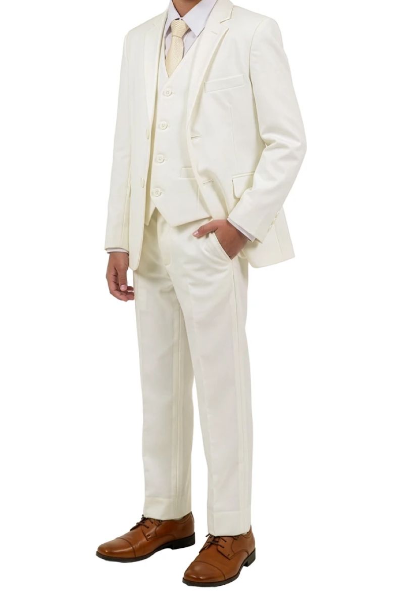 A boy wearing a five-piece cream-colored suit with a matching vest and trousers, a light dress shirt, a cream tie, and brown leather dress shoes, shown against a plain white background.