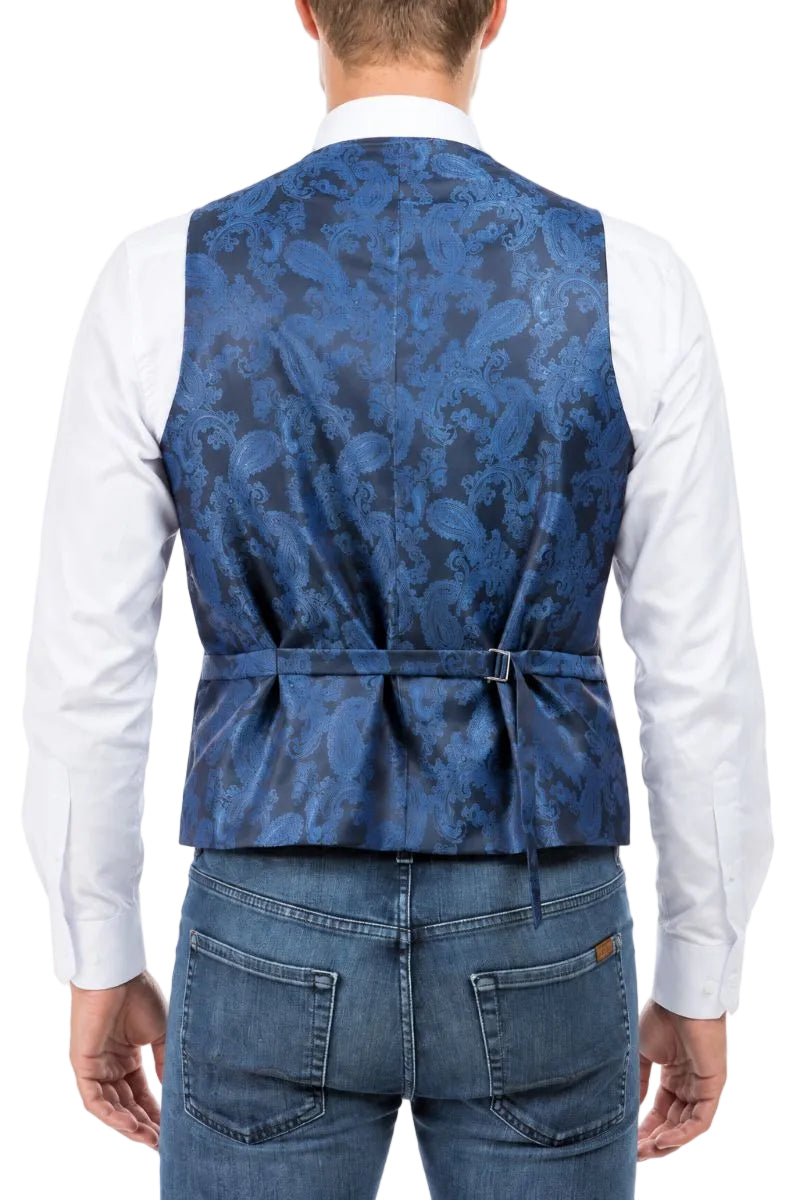 A man viewed from the back wearing a blue patterned waistcoat over a white long-sleeve shirt and blue jeans, against a plain white background.