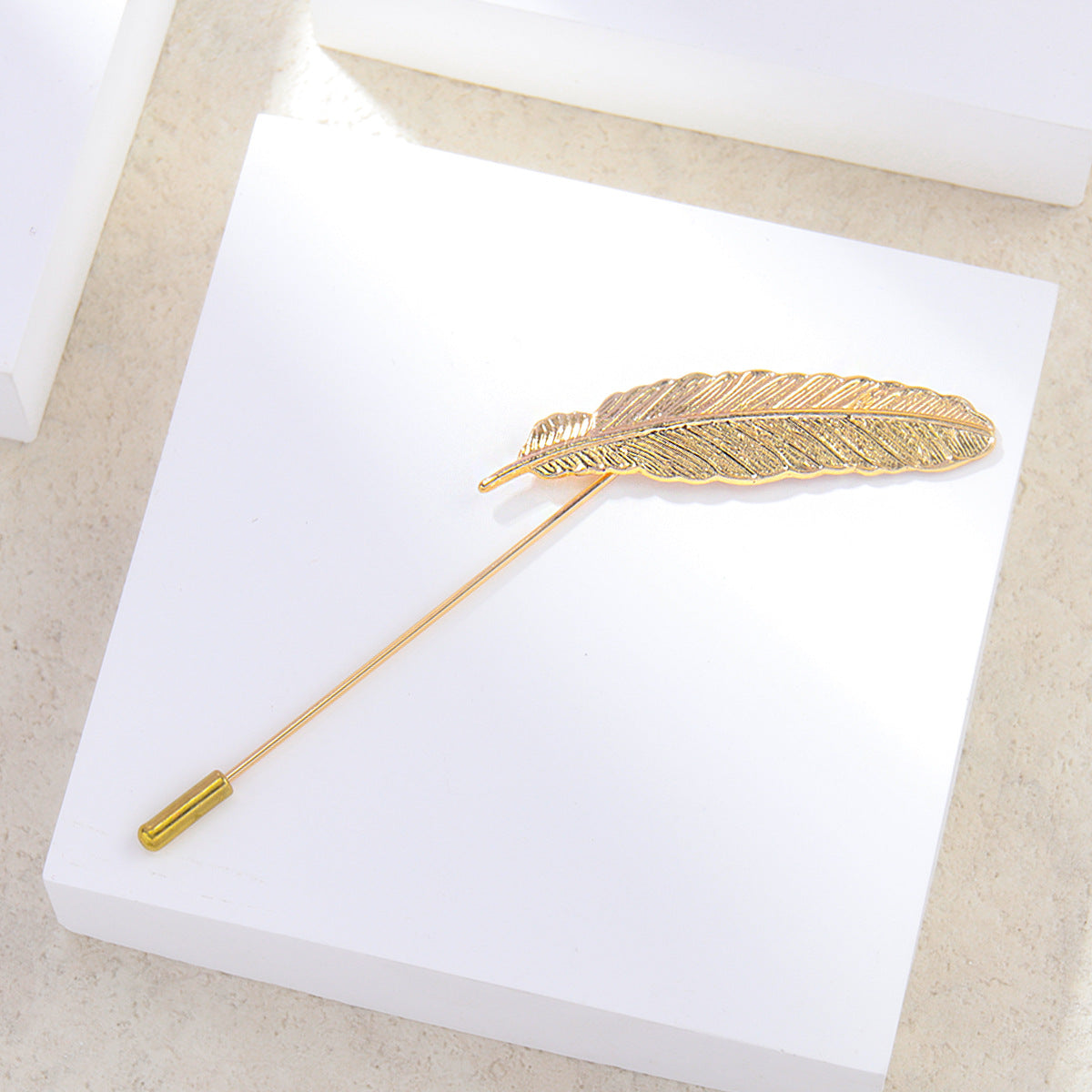 Gold feather-shaped lapel pin on a white card with a beige background