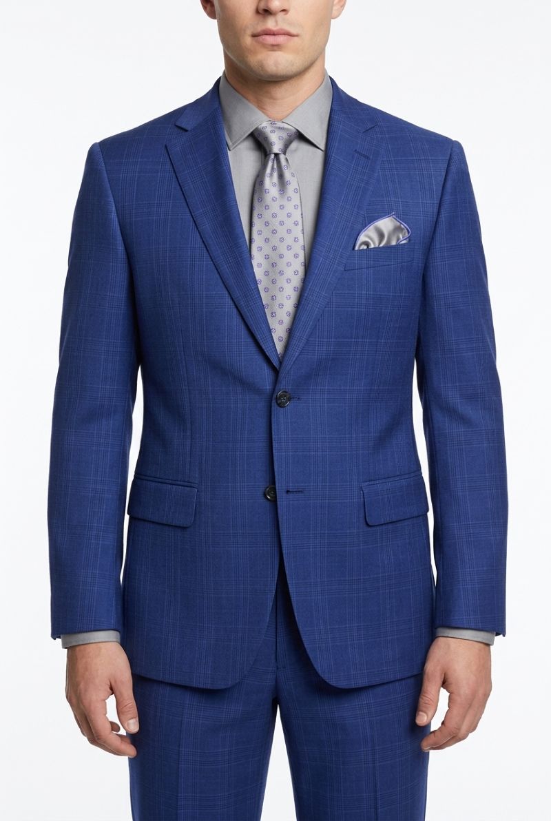 A man wearing a blue plaid suit jacket and matching trousers, styled with a light gray dress shirt, a patterned gray tie, and a matching pocket square, against a plain white background.