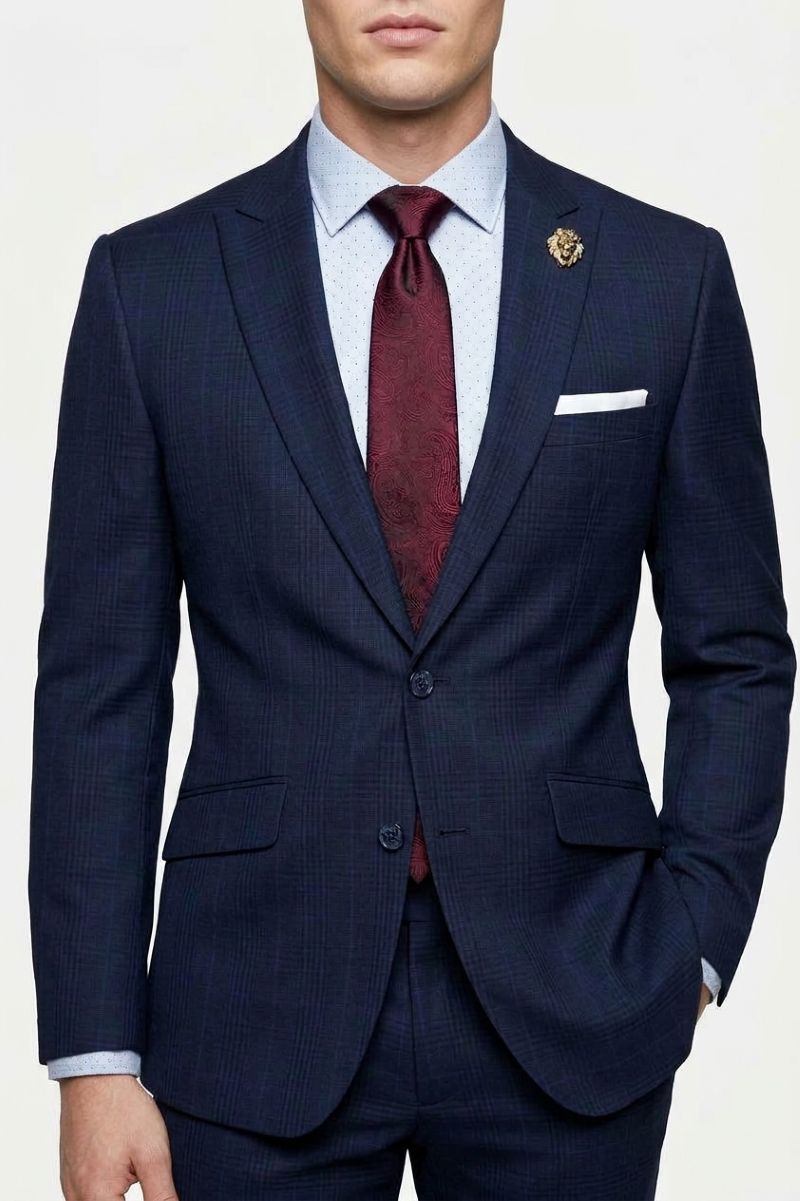 A man wearing a navy blue textured suit jacket with a light blue dress shirt, a burgundy tie, and a white pocket square, shown from the chin down on a white background.
