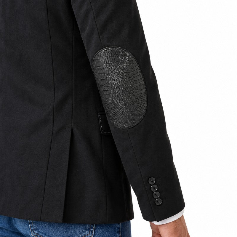 Close-up of a black blazer with textured crocodile-embossed elbow patches on the sleeve, shown on a model wearing blue jeans against a white background.