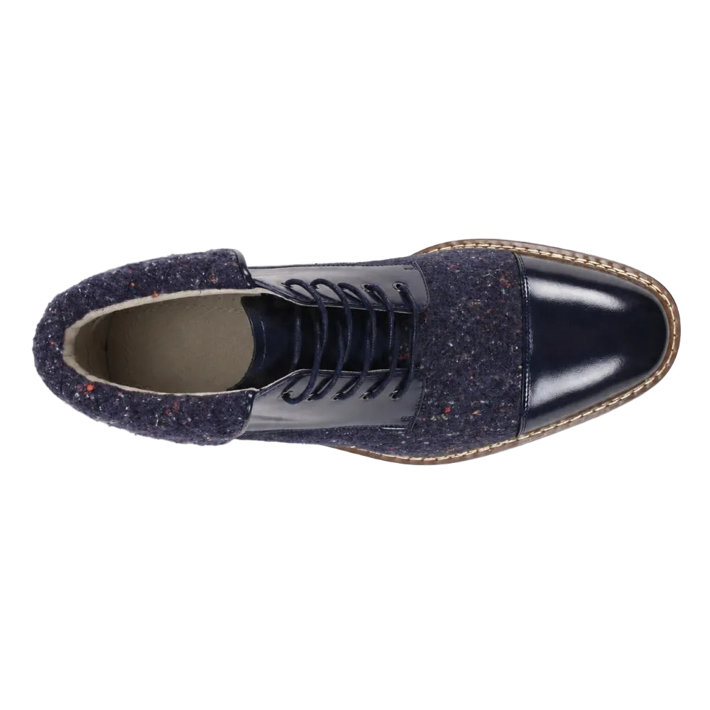 A single men's lace-up ankle boot shown from a top-down view on a white background. The boot features a glossy dark navy patent leather toe cap, a textured navy blue knit upper with subtle multicolor flecks, and a light tan braided welt around the edge of the sole.