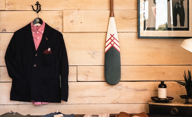 a men's blazer and dress shirt hanging on a hook next to a decorative paddle on a rustic wood-paneled wall