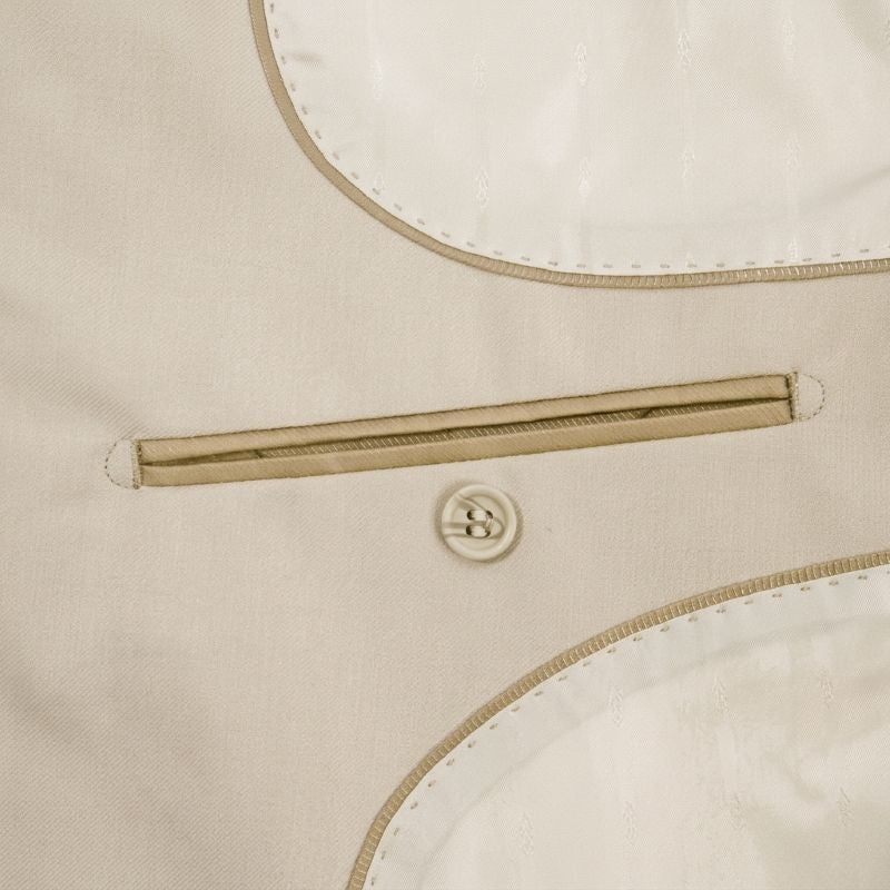 Close-up detail of a light beige or cream jacket fabric showing a diagonal zip pocket, a decorative button, and contrast stitching.