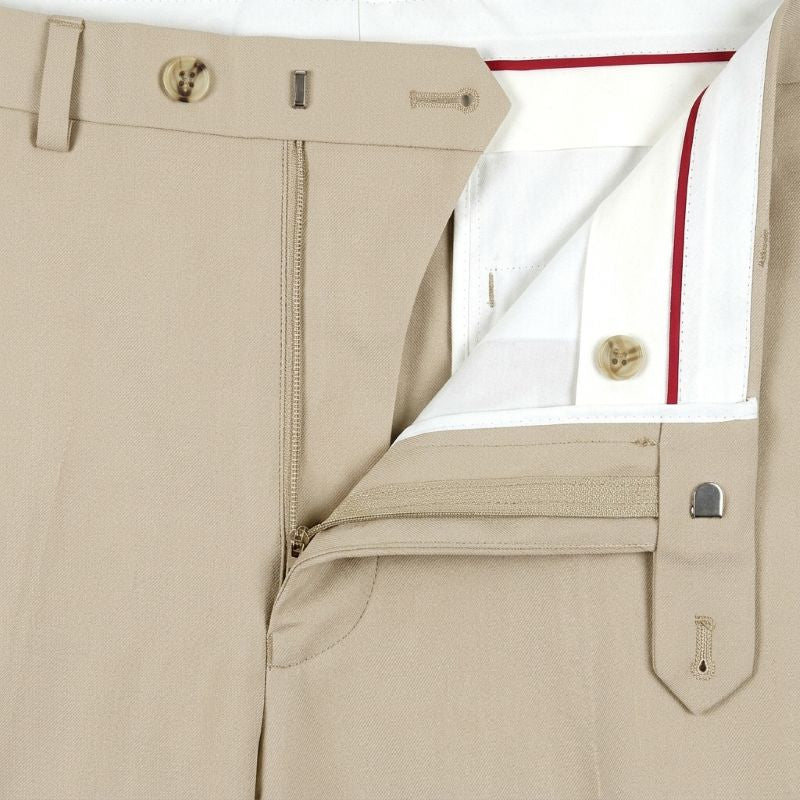 Close-up of beige tailored trousers showing the front zip fly, belt loops, button closure, and a folded white shirt with red piping tucked inside.