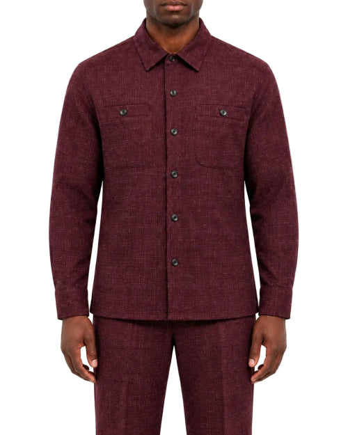 A man wearing a matching burgundy textured two-piece suit, featuring a long-sleeve button-up shirt jacket and coordinating trousers, shot against a plain white background.