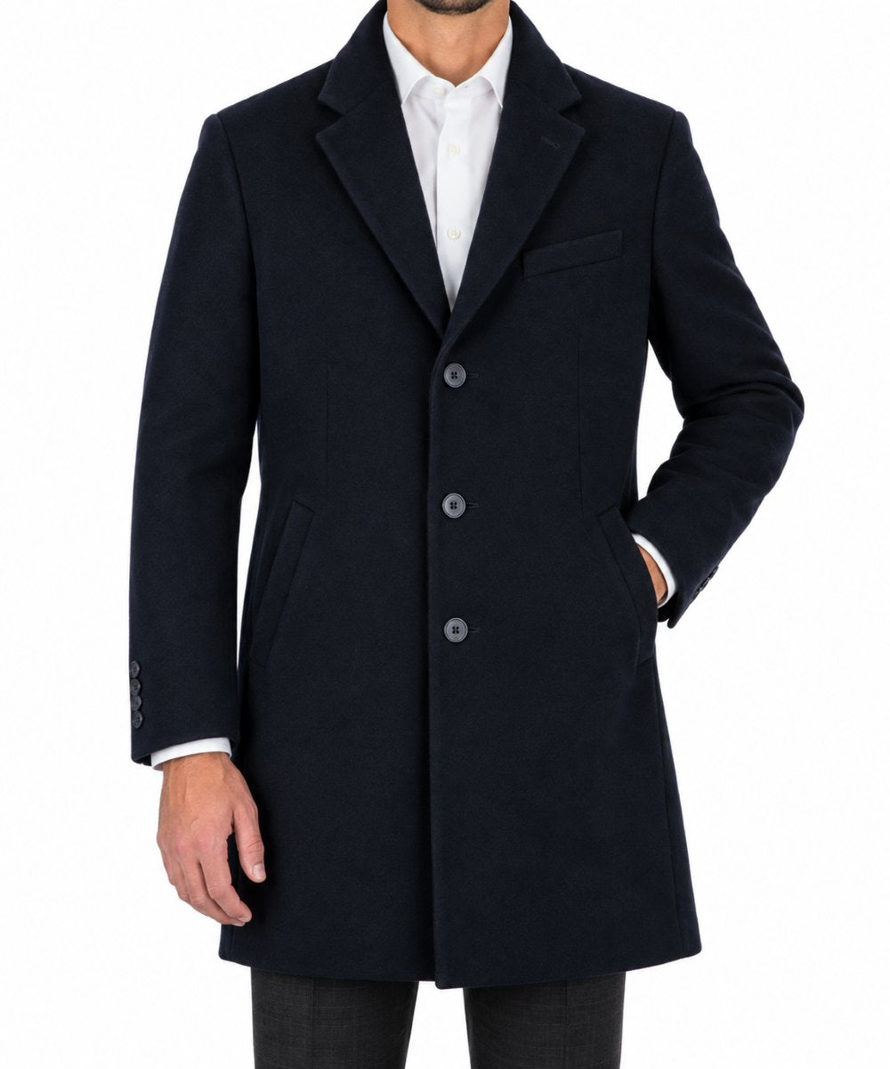 A man wearing a dark navy blue wool-blend overcoat over a white collared shirt, shown from the neck down against a plain white background.