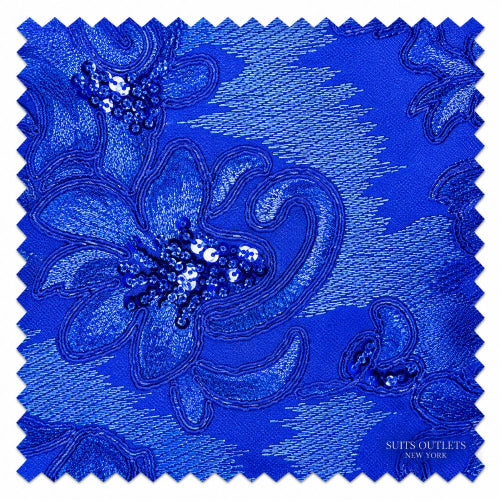 A square fabric swatch with serrated edges in vivid royal blue, featuring an ornate embroidered floral pattern with sequined details. The text 'SUITS OUTLETS NEW YORK' is printed in the bottom right corner.