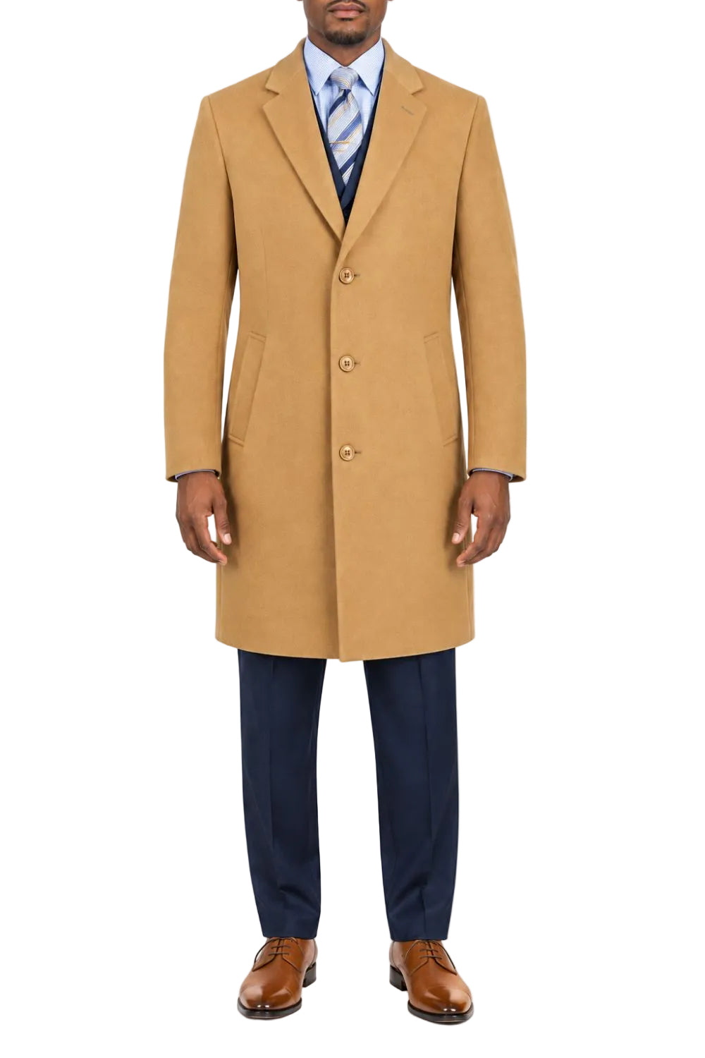 A man wearing a camel-colored wool-blend overcoat, navy blue trousers, a light blue dress shirt, a blue and white striped tie, and brown leather dress shoes, standing against a plain white background.