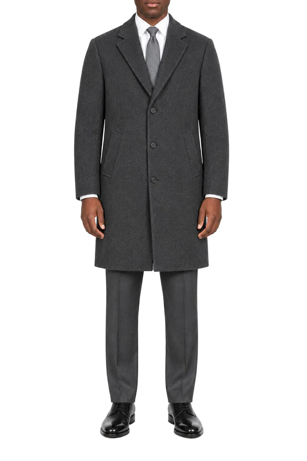 A man wearing a dark gray wool-blend overcoat, matching gray trousers, a white dress shirt, a gray tie, and black dress shoes, standing against a plain white studio background.