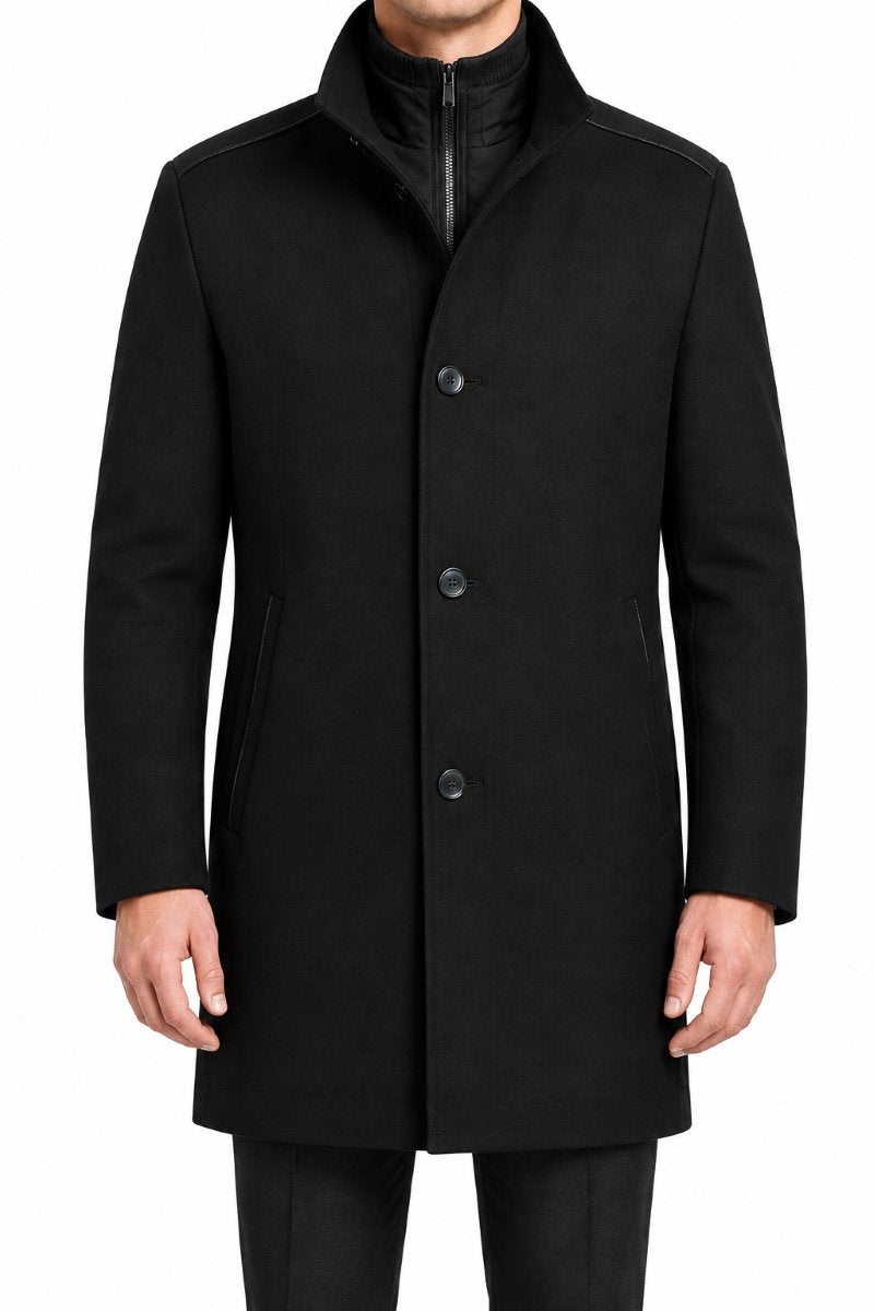 A man wearing a black mid-length coat with a high stand collar, three front buttons, and side pockets, photographed against a plain white background.