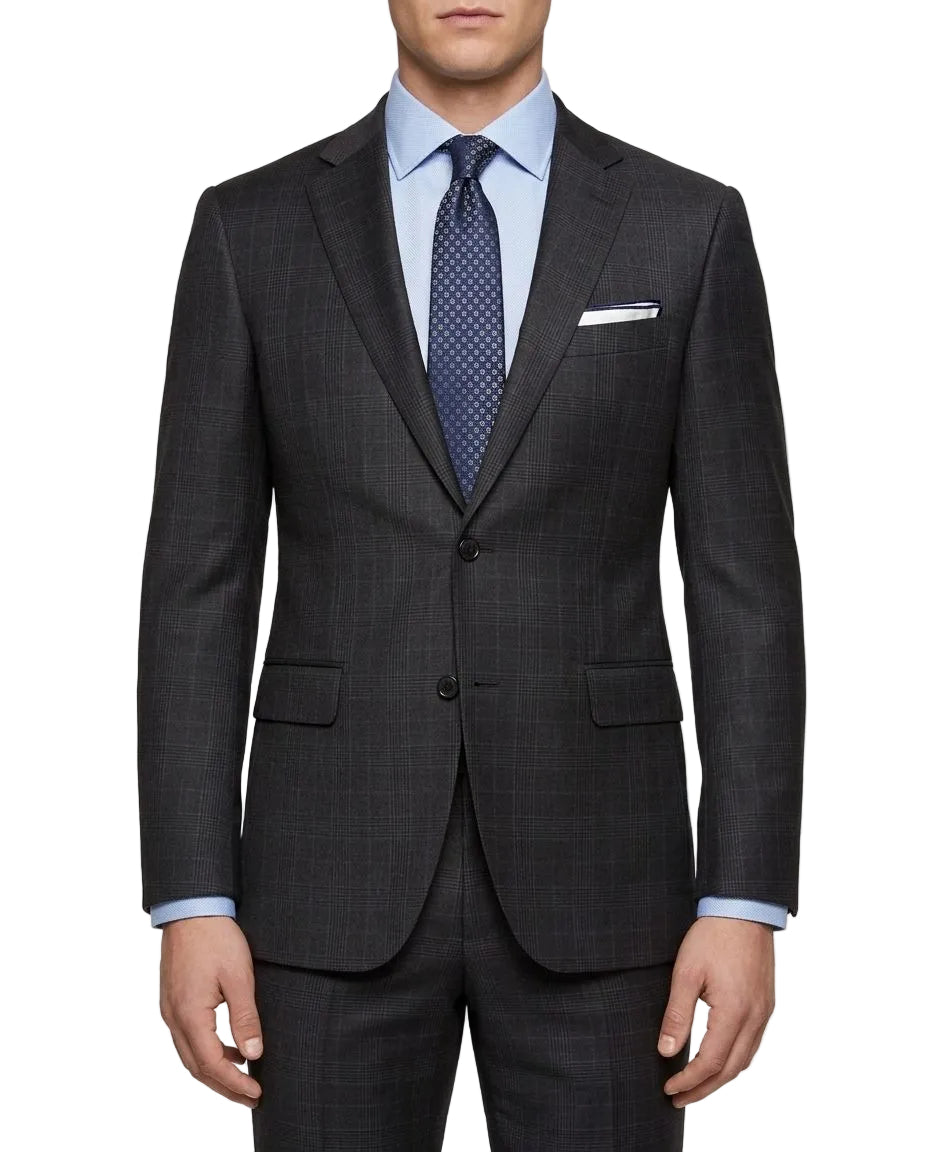 A man wearing a dark charcoal gray windowpane plaid suit jacket with matching trousers, styled with a light blue dress shirt and a navy patterned tie, against a plain white background.