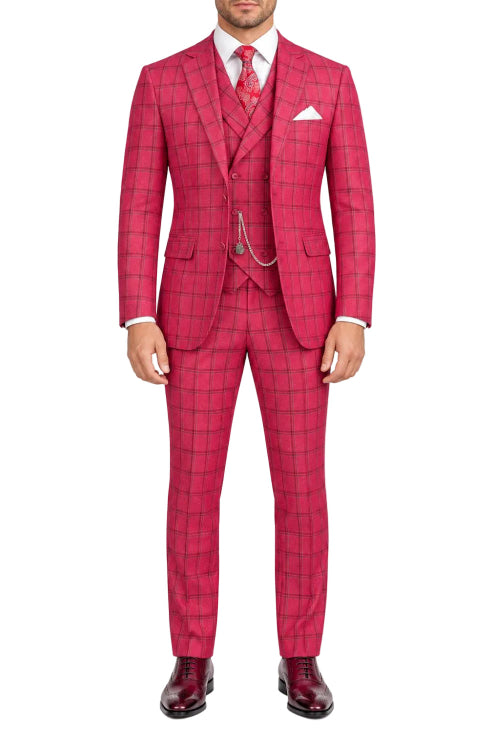 A man wearing a bright pink three-piece suit with a subtle windowpane plaid pattern, paired with a white dress shirt, a red patterned tie, and dark burgundy dress shoes, photographed against a solid white background.