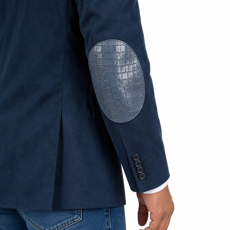 Close-up of a navy blue blazer with a textured gray crocodile-embossed elbow patch on the sleeve, worn by a model with blue jeans against a white background.