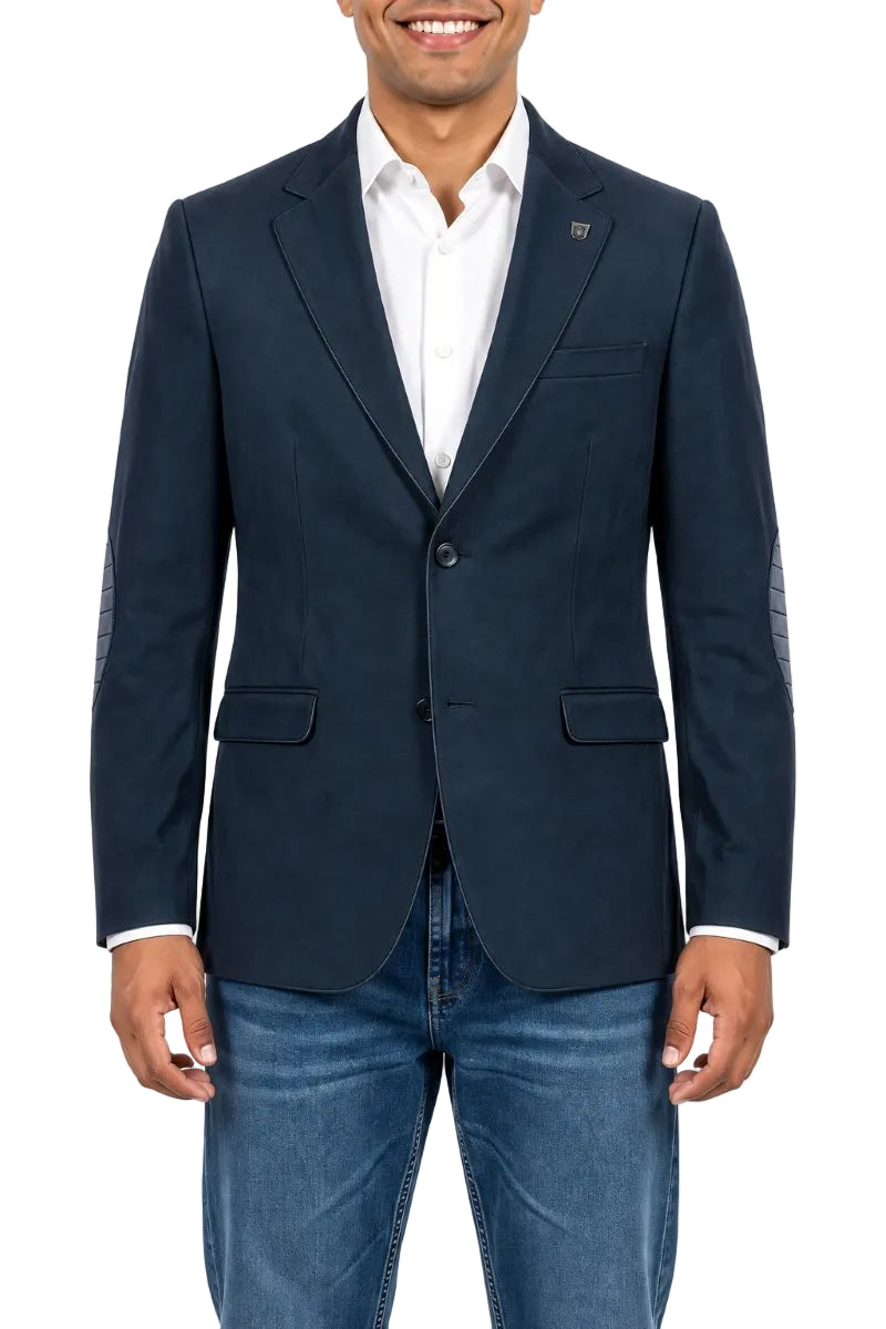 A man wearing a navy blue blazer with textured knit elbow patches, a white dress shirt, and blue jeans, shown from the waist up against a white background.