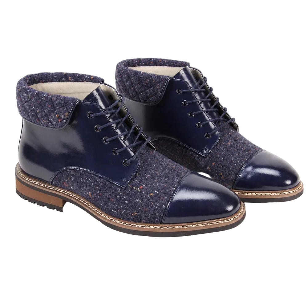 A pair of men's lace-up ankle boots in navy blue, featuring a glossy patent leather toe cap and side panels, textured tweed fabric uppers, quilted collar lining, and brown stacked soles.