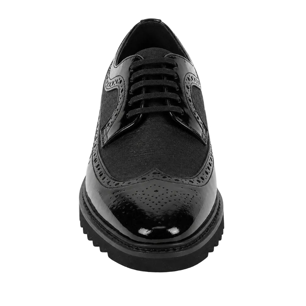 A black brogue oxford shoe with a textured fabric upper, glossy patent leather toe cap, and a chunky lug sole, shown from a front-facing perspective on a white background.