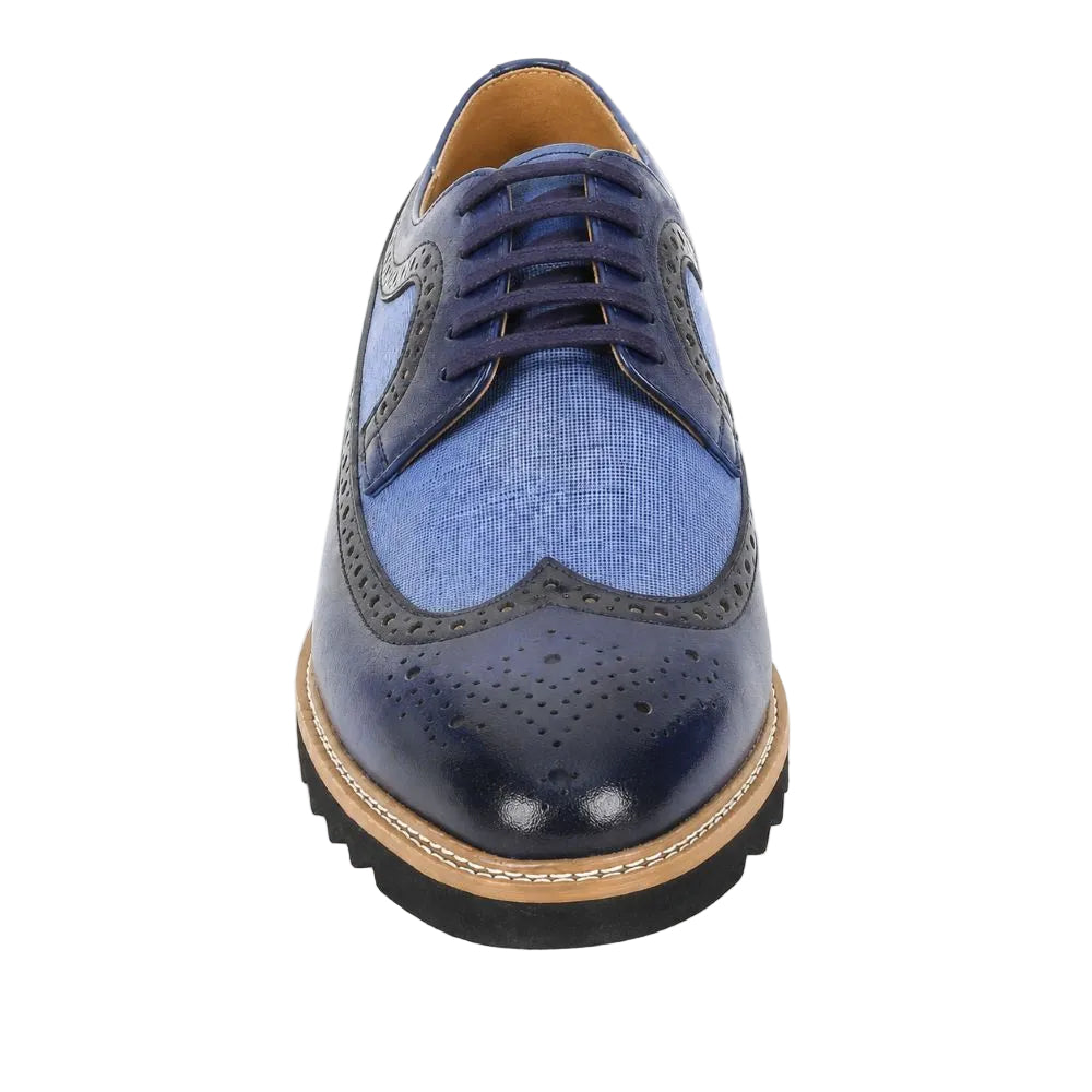 A men's wingtip oxford shoe featuring a textured medium blue suede vamp, dark navy leather toe cap with perforations, navy laces, and a tan welt on a black sole, shown from a front-facing perspective on a white background.