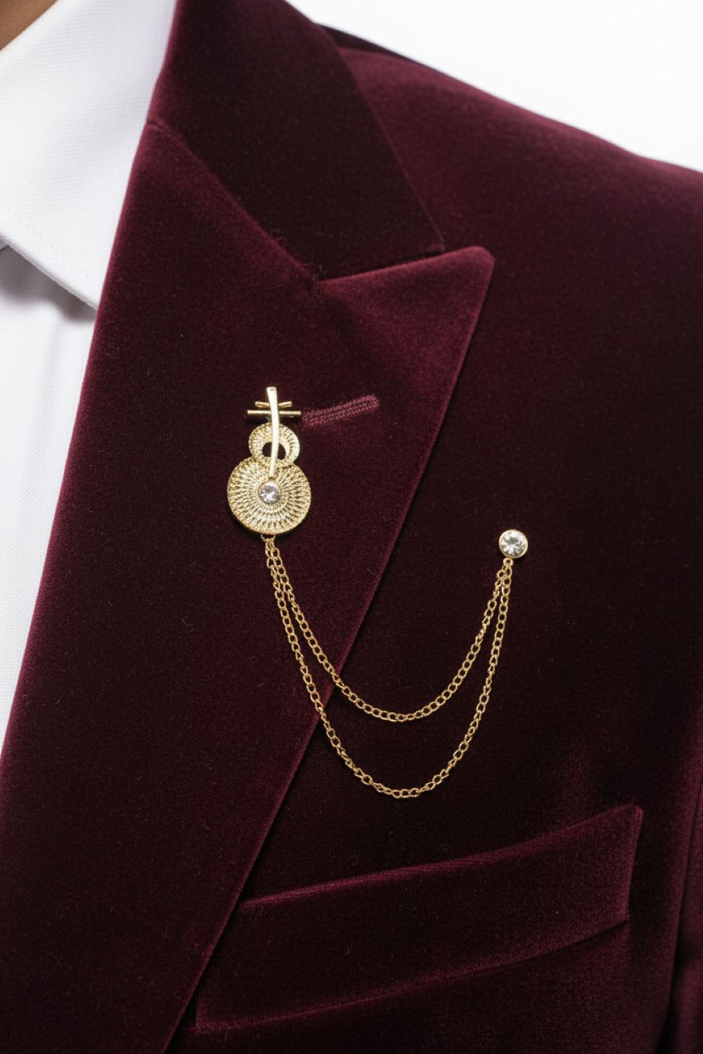 Gold brooch with chain on a burgundy blazer against a white background