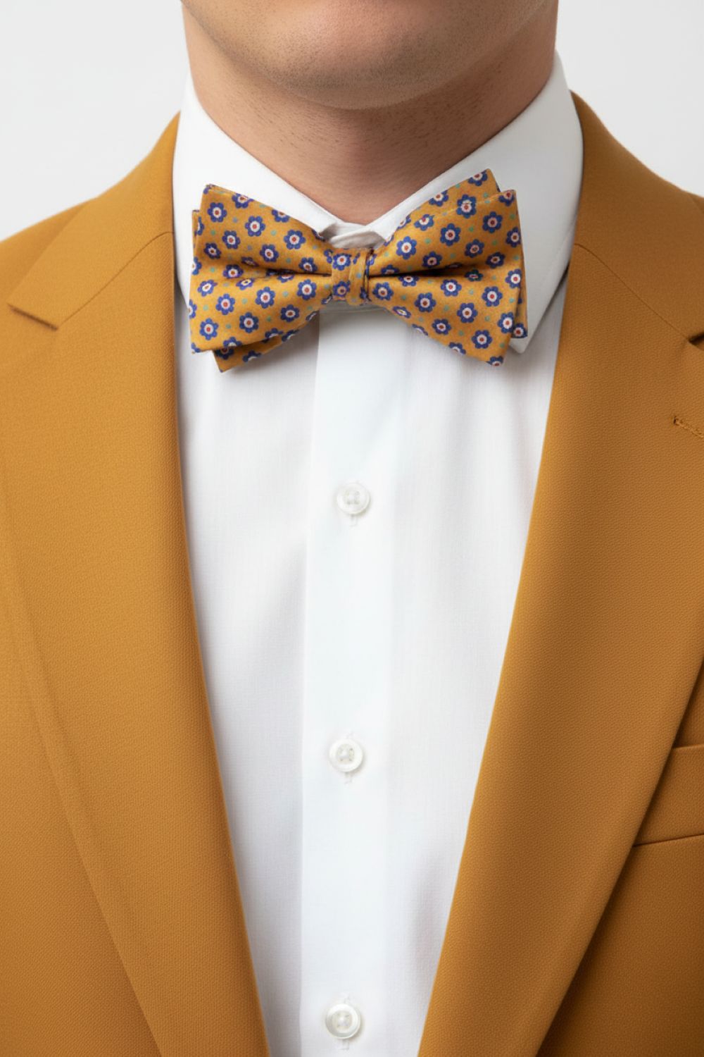 Man wearing a mustard yellow suit with a patterned bow tie against a white background
