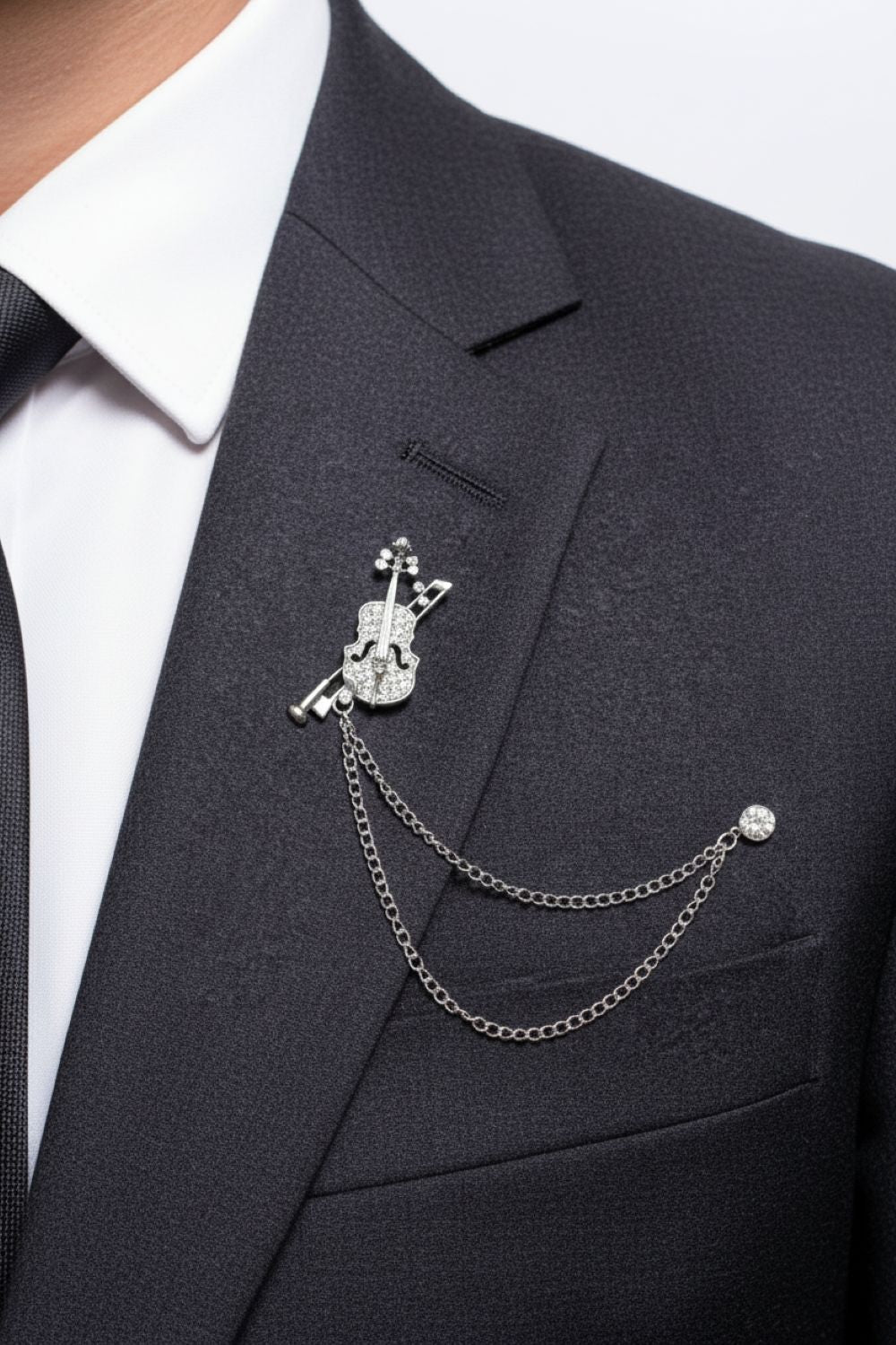 Black suit jacket with a decorative lapel pin featuring a chain on a white background